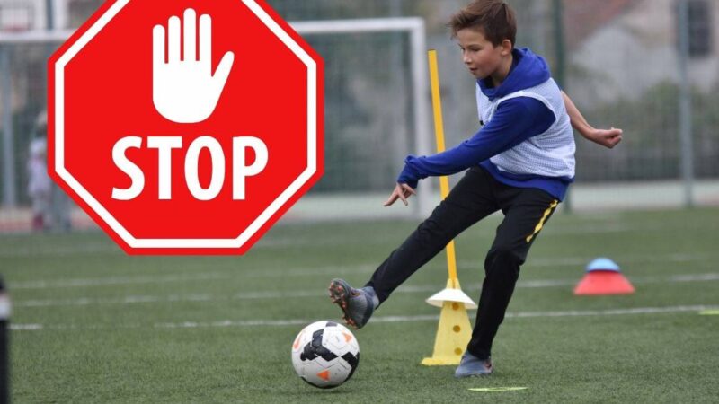 chłopiec kopiący piłkę, obok znak stop