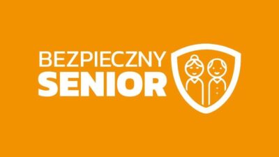 Logo programu Bezpieczny Senior, biały napis na pomarańczowym tle, na tarczy widnieje wizerunek dwóch starszych osób - kobiety i mężczyzny.