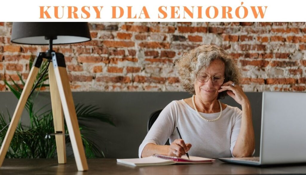 Na zdjęciu widoczna seniorka, która siedzi przed laptopem, w jednej ręce trzyma długopis i notuje w zeszycie.