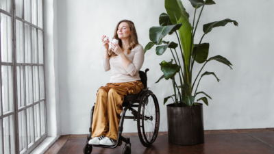 kobieta na wózku inwalidzkim, obok duży kwiat doniczkowy