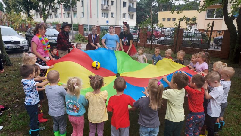 dzieci i wolontariuszki bawią się kolorową chustą animacyjną
